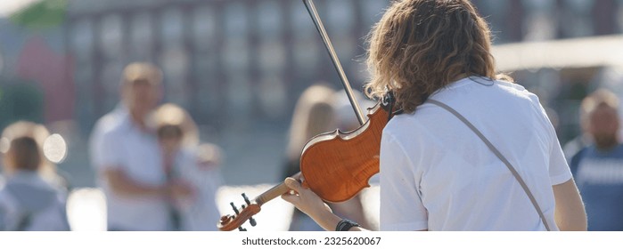 Photography of a street musician plays the violin on a city street in a summer day. Young woman. Her hair is curly.  Back, rear view. Festive mood. Live music