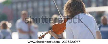 Photography of a street musician plays the violin on a city street in a summer day. Young woman. Her hair is curly.  Back, rear view. Festive mood. Live music