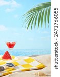 The photography of summer picnic on beach from front view, a checkered yellow carpet on sand seaside contains a glasses, a watermelon piece and juice, still blank space for product presentation