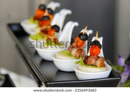 a photography of a table with a row of small dishes of food, plate of appetizers with meat and vegetables on a black tray.
