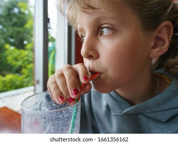 Photography of a teenager girl drinking a milkshake through a straw and looking out the window in summer. Her nails are painted pink. She is thoughtful and attentive. Lifestyel concepts. - Powered by Shutterstock