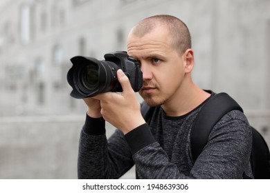Photography And Tourism Concept - Handsome Male Photographer Taking Photo With Modern Dslr Camera Over Concrete Building Background
