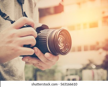 Photography or traveler Concept.The photographer hold DSRL camera in his hands with cityscape blur background and sunlight in summer time, selective focus. Photo of Vintage and filtered process. - Shutterstock ID 563166610