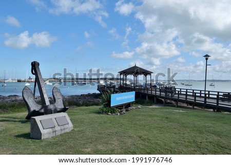 Photography of a wooden pier and a gazebo and the boats anchored at  the port of Punta del Este City, Uruguay and a sign saying Port of Punta del Este in spanish and an anchor
