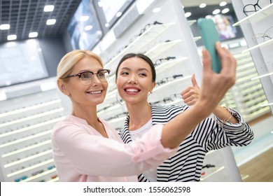 Photos With Assistant. Smiling Blonde-haired Woman Taking Photos With Shop Assistant In An Optical Store