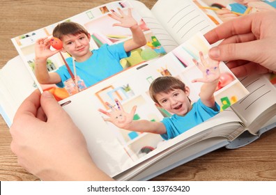 Photos In Hands And Photo Album On Wooden Table