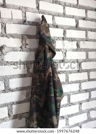 Photos from the side of the Army jacket hanging on the white stone wall.