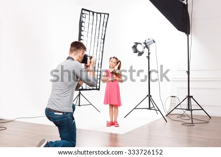 Photoshoot in progress. Young handsome male photographer in the process of taking photos of small model girl.