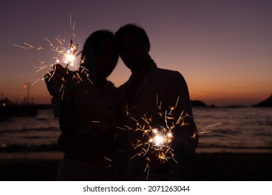 Photoshoot of young helthy beautiful caucasian couple, boy and girl lovers , dating at the beach - Man and woman celebrate New Year's Eve in holidays near the ocean with fireworks