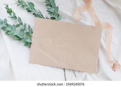 Photostock wedding styled composition. Feminine desktop mockup scene with leaves, silk ribbon, blank greeting card on white textured fabric background. Flat lay, top view.