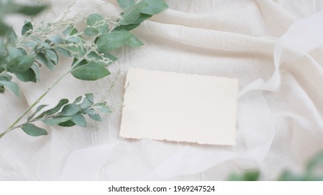 Photostock wedding styled composition. Feminine desktop mockup scene with leaves, silk ribbon, blank greeting card on creme textured fabric background. Flat lay, top view.
