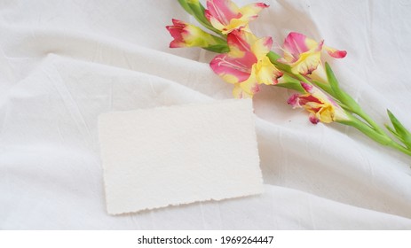 Photostock wedding styled composition. Feminine desktop mockup scene with leaves, Amaryllis flower, silk ribbon, blank brown greeting card on white textured fabric background. Flat lay, top view.