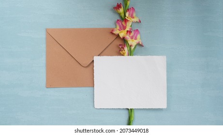 Photostock wedding styled composition. Feminine paper mockup scene with Amaryllis flower, silk ribbon, brown envelope, blank greeting card on Tosca textured concrete background. Flat lay, top view