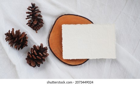 Photostock wedding styled composition. Feminine square recycled paper mockup scene wooden tray with pinecone on white textured fabric background. Flat lay, top view.