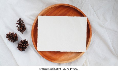 Photostock wedding styled composition. Feminine square recycled paper mockup scene wooden plate with pinecone on white textured fabric background. Flat lay, top view