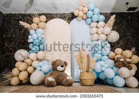 Photo-wall decoration space or place with beige, brown, blue balloons. Celebration baptism concept. Birthday party for boy. Trendy autumn decor with dry leaves. Arch with bears on background balloons.