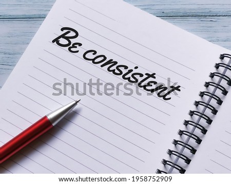 Phrase be consistent written on notebook with a pen.