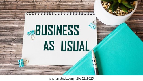 The phrase Business as usual on a notepad and a diary with a pen on a wooden table. - Shutterstock ID 2065219625