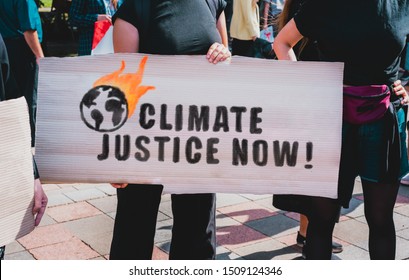 The phrase " Climate justice now " drawn on a carton banner in woman's hand. Protest for ecology. Human holds a cardboard with an inscription: Climate justice now - Powered by Shutterstock