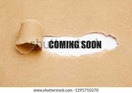 The phrase Coming Soon appearing behind ripped brown paper. Concept about upcoming promising event approaching in near future.