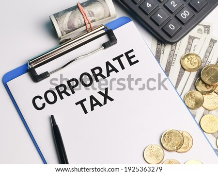 Phrase CORPORATE TAX written on paper clipboard with calculator,a pen,coins and fake money. Business and finance concept.
