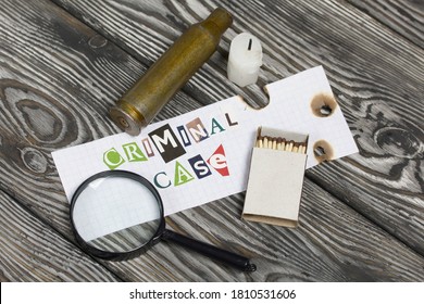 The Phrase Criminal Case Made Of Letters Cut From A Magazine And Pasted On A Sheet Of Paper. Nearby Lies A Spent Cartridge Case And A Magnifying Glass. There Is A Candle Stub And A Box Of Matches.