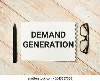 Phrase Demand Generation Written On Note Book With A Marker Pen And Eye Glasses.