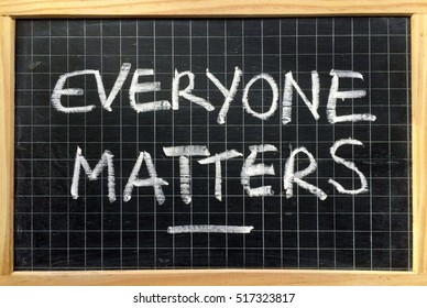 The phrase Everyone Matters written by hand in white chalk on a used blackboard as a reminder of equality for all