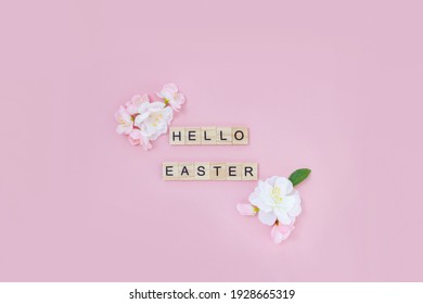 Phrase Hello Easter laid out from wooden letters on pink background and decorated with spring flowers. Flat lay, top view