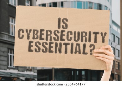 The phrase 'Is Cybersecurity Essential?' on a banner in a person's hand. Human holds a cardboard with an inscription. Protection. Privacy. Defense. Safety. Encryption. Technology. Awareness