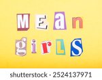 Phrase Mean Girls spelled in cut out newspaper style typography, isolated on yellow background.