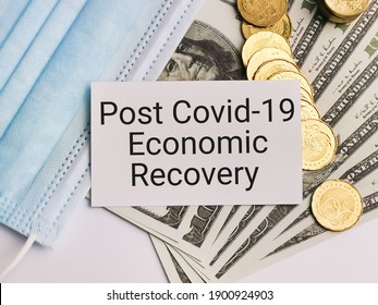 Phrase POST COVID 19 ECONOMIC RECOVERY On Note Book With Dollar Bank Notes, Coins And Face Mask. Covid-19 And Business Concept.