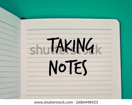 The phrase 'TAKING NOTES' is handwritten in bold, black marker on the lined page of an open notebook symbolizes active learning, writing, and documentation.