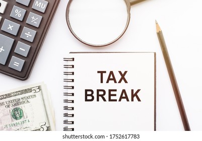 The Phrase Tax Break In Notebook With Calculator, Magnifier, Money And Pen Background On White Table. Business And Financial Concept