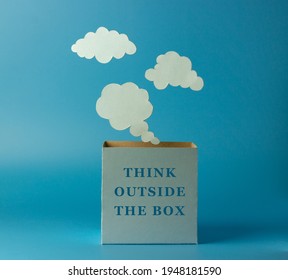 Phrase - think outside the box. Box and clouds or thoughts made of paper on a blue background. Concept to think imaginatively using new ideas instead of traditional ideas.