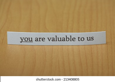 The phrase you are valuable to us typed on a strip of paper and left standing on a wooden desktop