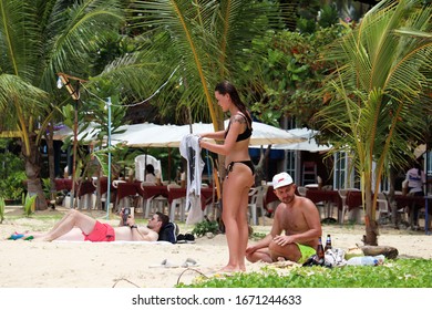 Phuket, Thailand - March 2020: Couple Relaxing On The Beach With Palms. Guy In Cap And Girl In Bikini Resting With Alchohol Drinks, Leisure On Paradise Resort