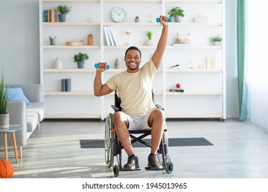 Physical activities for disabled people. Handicapped black man in wheelchair making rehabilitation exerises with dumbbells at home. Impaired young guy working out with weights indoors - Powered by Shutterstock