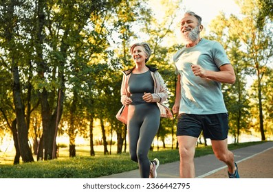 Physical activity of pensioners. Enthusiastic mature couple of husband and wife competing together and running race in park. Male and female keeping fit through regular and active training outdoors. - Powered by Shutterstock