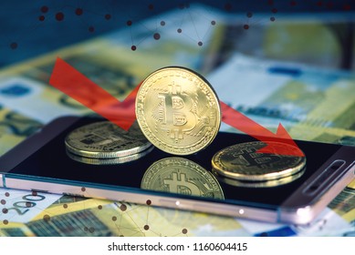 Physical bitcoin coin on the phone screen on the background of the Euro banknotes. Red arrow of the chart of falling quotes down - Shutterstock ID 1160604415
