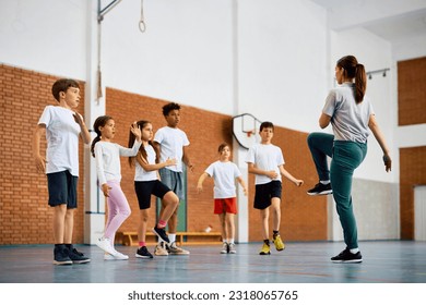 Physical education teacher and group of school children exercising during a class at school gym. Copy space. 