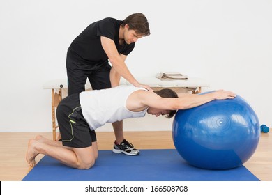 Physical Therapist Assisting Young Man With Yoga Ball In The Gym At Hospital