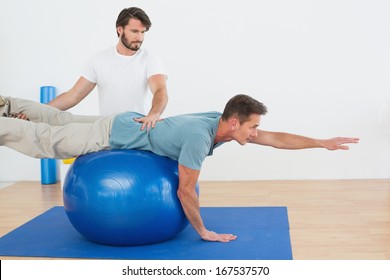 Physical therapist assisting young man with yoga ball in the gym at hospital