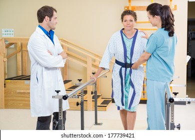 Physical therapist with doctor assisting female patient in walking with the support of bars