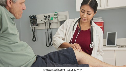 Physical Therapist Or Doctor With Older Male Patient In Exam Room Checking Range Of Motion On Knee Injury. Senior Man With Hurt Knee Getting It Checked By Female Medical Professional