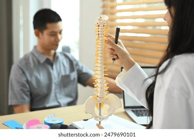 Physical therapist educating male patient with spinal model at consultation room. - Powered by Shutterstock