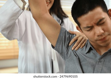 Physical therapist helping male patient doing stretching exercises, shoulder joint treatment. - Powered by Shutterstock