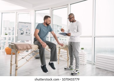 Physical Therapist. Nice Smart Doctor Talking To His Patient While Taking Notes