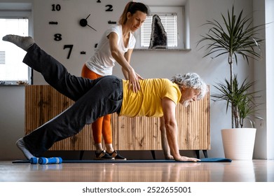 Physical therapist or personal trainer working with a senior man to execute plank exercise with correct posture for a healthy ageing and injury recovery. At home visit in a domestic living room.  - Powered by Shutterstock