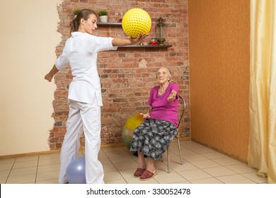 Physical Therapist Showing Exercise With Spiky Ball For Senior Woman Sitting On A Chair